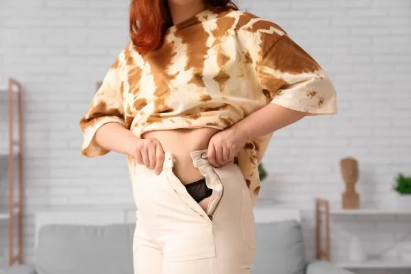 Image of woman trying to do her trousers up after pregnancy weight gain Billericay