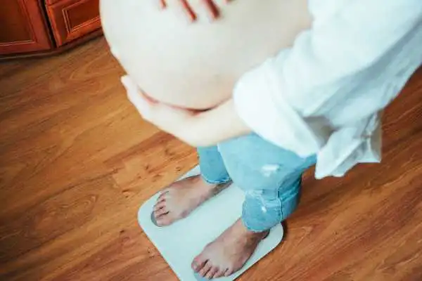 Image of woman weighing herself and experiencing weight gain through pregnancy Billericay